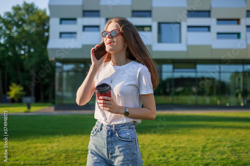 a student near the school in her free time talking on the phone holding a glass of coffee in her hands. © Ivan