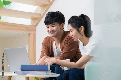 Asian woman and man working on laptop while sitting on the sofa. Woman giving man a thumb up.