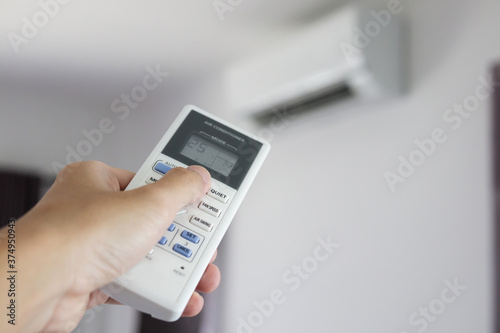 Hand with remote control directed on air conditioner inside the room