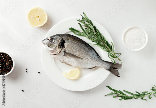 Raw dorado with lemon, pepper and rosemary on a plate, top view.