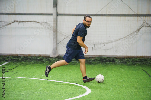 man playing football indoor on green lawn on soccer arena. Amateur sport