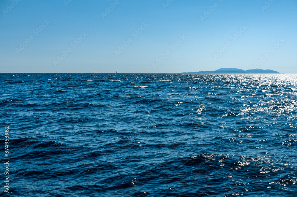 Fototapeta premium Deep blue sea horizon. Waves on the sea with island on horizon.