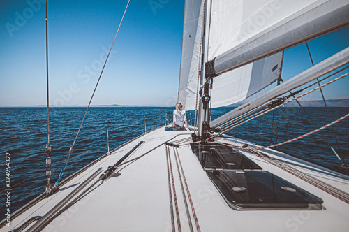 Beautiful girl on sailing ship yacht with white sails in open sea. Luxury boat on ocean with wind in sails and woman on board.