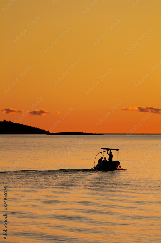 Fishermen on the adriatic sea at orange sunset in Croatia