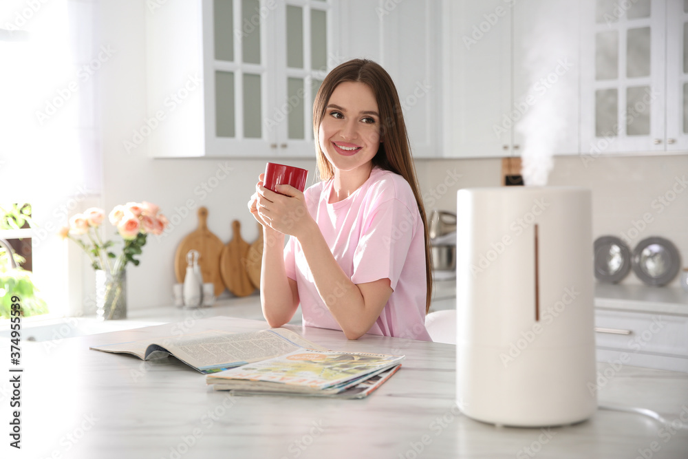 Woman drinking coffee in kitchen with modern air humidifier Woman drinking coffee in kitchen with modern air humidifier