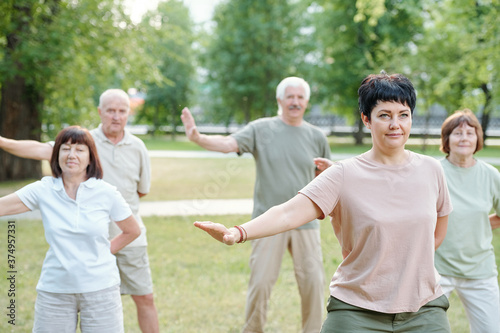 Active mature people standing in park and moving arms at qigong practice © pressmaster