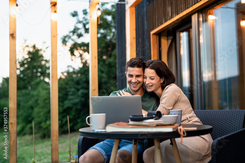 Young couple with laptop outdoors, weekend away in container house in countryside.
