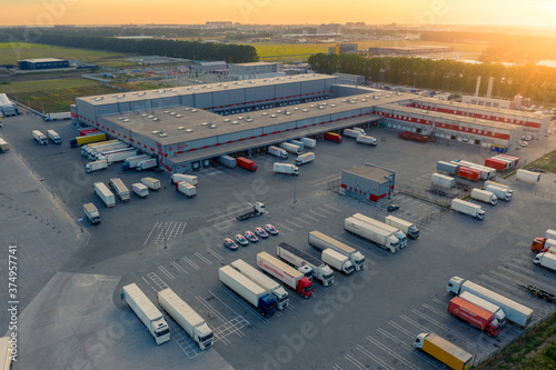 Aerial view of the logistics park with warehouse, loading hub and many semi trucks with cargo trailers standing at the ramps for load/unload goods at sunset photo