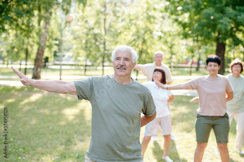 Handsome senior man with mustache practicing qigong exercise to be healthy and calm at group class in park