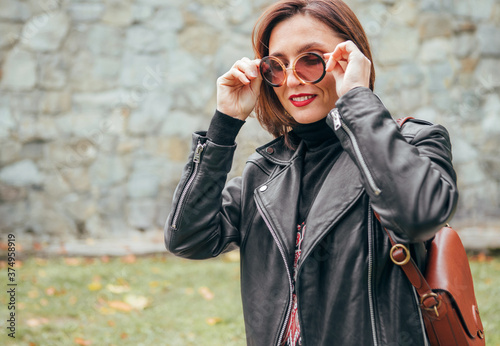 Fotografía .Smiling female dressed boho fashion style in a black leather biker jacket with