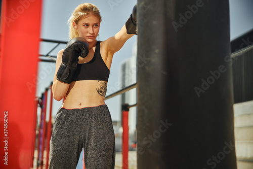 Sportive beautiful woman punching by left boxing glove during a kikcboxing training in the sport ground