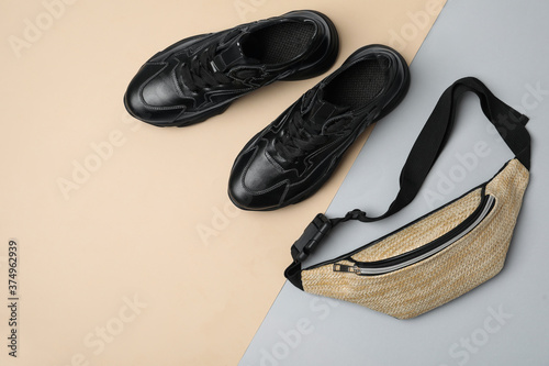 Fényképezés Stylish black sneakers and fanny pack on color background, flat lay