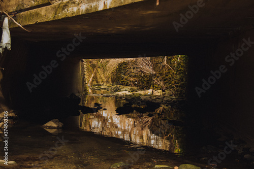 A Shallow Creek Flowing Under a Concrete Bridge Surrounded by Foliage and Rocks