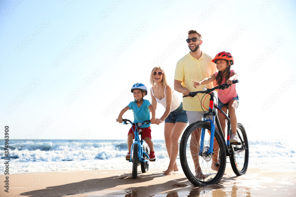Fototapeta premium Happy parents teaching children to ride bicycles on sandy beach near sea