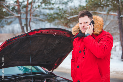 man standing near broken car with opened hood calling help