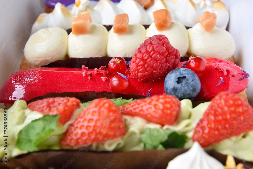 Tasty French eclairs with icing, cream, fresh berries and sugar decor elements. Set of delicious eclairs with creative colorful decor in white paper box. Tasty French eclairs with icing, cream, fresh berries and sugar decor elements. Set of delicious eclairs with creative colorful decor in white paper box.