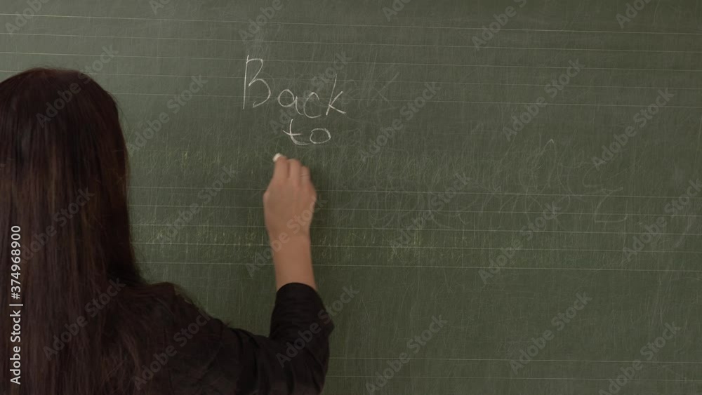 A young teacher writes on a blackboard back to school, turns and takes off her medical mask.4k A young teacher writes on a blackboard back to school, turns and takes off her medical mask.4k