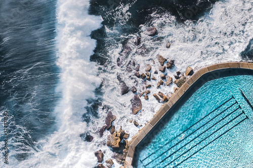 Aerial View Of Large Ocean Waves Breaking Towards Natural Water Coastal Swimming Pool With Person Swimming In Bronte, Sydney, Australia photo