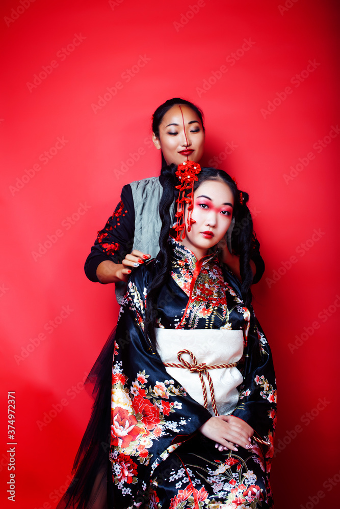 two pretty geisha girls friends: modern asian woman and traditional wearing kimono posing cheerful on red background two pretty geisha girls friends: modern asian woman and traditional wearing kimono posing cheerful on red background