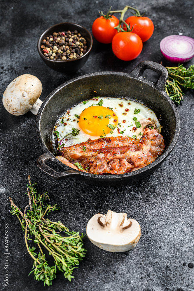 English breakfast, fried egg, tomatoes, mushrooms, bacon. Black background. Top view