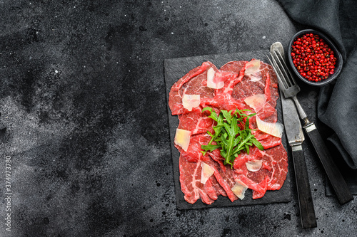 Beef carpaccio on black plate with parmesan cheese and arugula. Black background. Top view. Copy space.