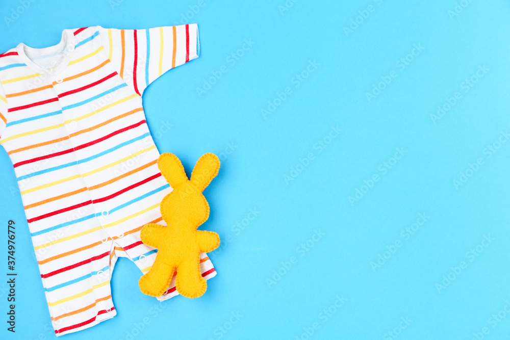 Baby clothes with soft rabbit toy on blue background
