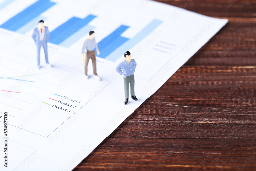 Miniature people and financial papers with graph and charts on brown wooden table Miniature people and financial papers with graph and charts on brown wooden table