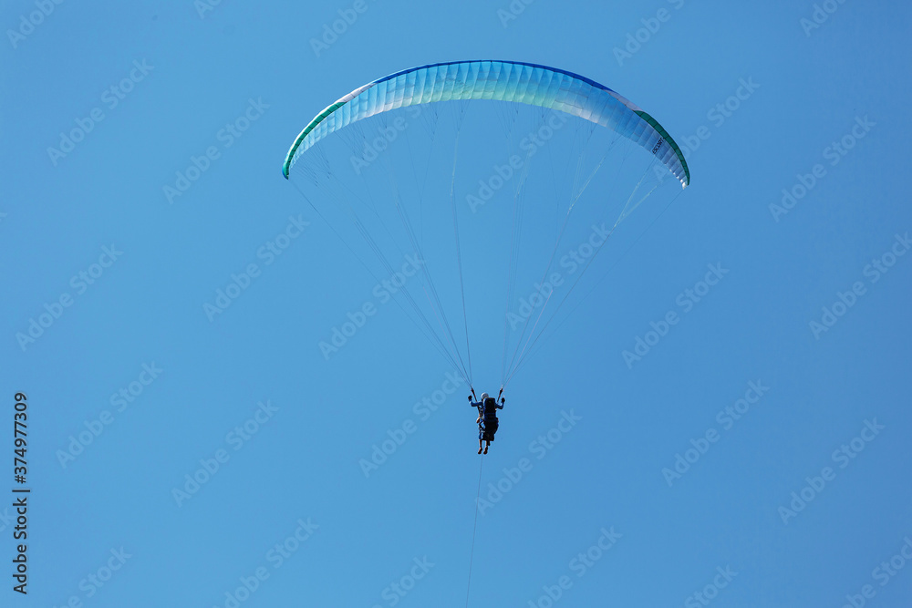 Blue Paraglider flying into the sky with clouds on a sunny day Blue Paraglider flying into the sky with clouds on a sunny day