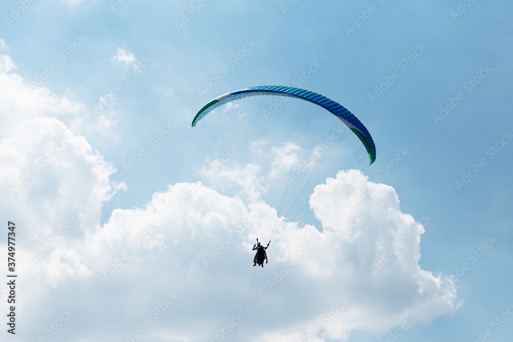 Blue Paraglider flying into the sky with clouds on a sunny day Blue Paraglider flying into the sky with clouds on a sunny day