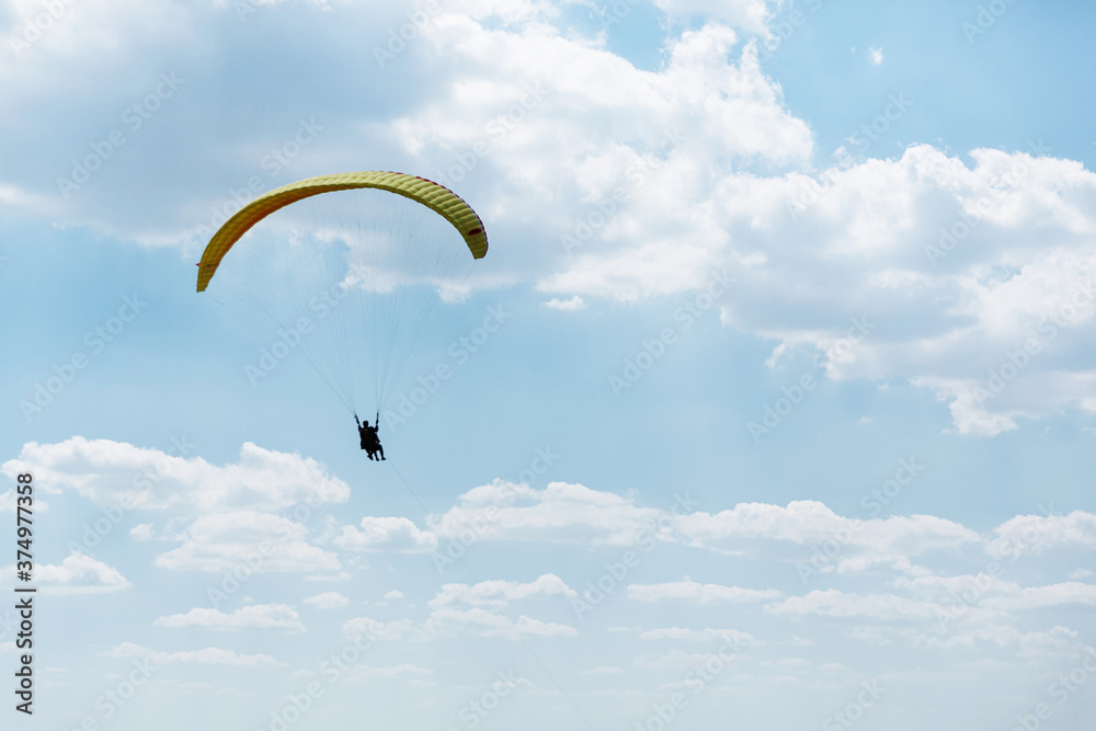 Yellow Paraglider flying into the sky with clouds on a sunny day Yellow Paraglider flying into the sky with clouds on a sunny day