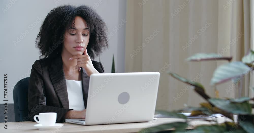 Pensive girl sits at home at table with laptop, processes information, frowns serious young face, solves difficult problem, test, conducts analysis, research online on Internet, looking for solution