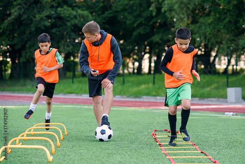 Active teen footballers train together on artificial soccer field and follow the instructions of a professional coach. © gorynvd