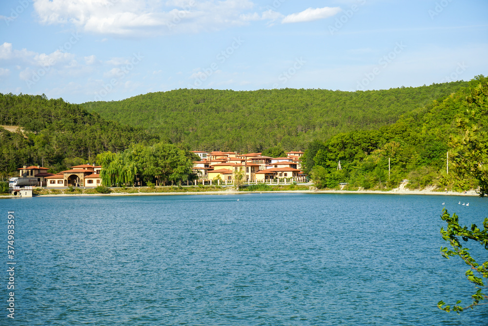 Lake Abrau Dyurso against the background of mountains, blue sky and beautiful white clouds and a view of the resort complex of buildings in the gorge, immersed in dense green vegetation
