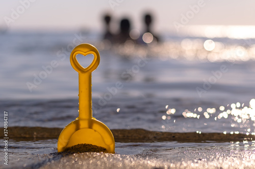 Vacation time, yellow toy shovel with heart symbol in front of the children in the sea, tourism concept
