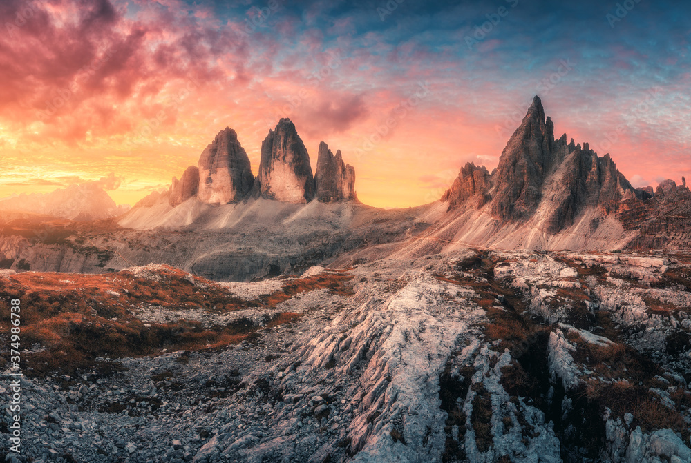Mountains and beautiful sky with colorful clouds at sunset. Autumn landscape with mountains, stones, grass, sky with red and orange clouds. High rocks in fall. Tre Cime in Dolomites, Italy. Travel