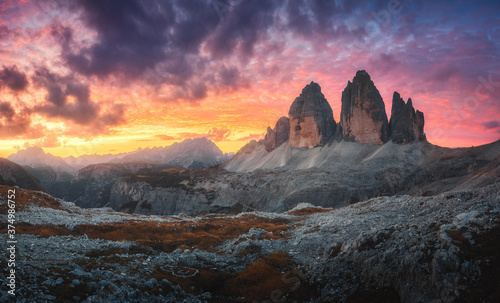 Mountains and beautiful sky with colorful clouds at sunset. Autumn landscape with mountains, stones, grass, sky with red and orange clouds. High rocks in fall. Tre Cime in Dolomites, Italy. Travel