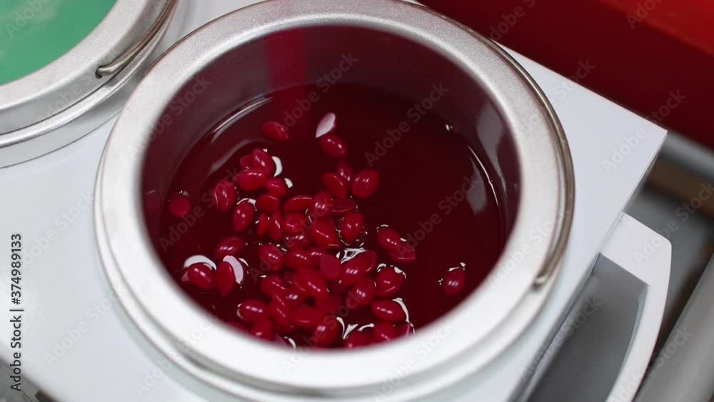 Red granules of depilatory wax are poured into the wax melting device. Preparation for the procedure for removing unwanted hair. Sugaring. Depilation. Epilation. Beauty Concept. Red granules of depilatory wax are poured into the wax melting device. Preparation for the procedure for removing unwanted hair. Sugaring. Depilation. Epilation. Beauty Concept.