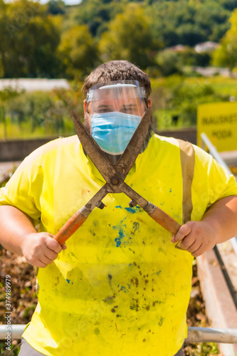 Worker in a recycling factory or clean point and garbage with a face mask and plastic protective screen, new normal, coronavirus pandemic, covid-19. Portrait with reflective vest and giant scissors photo