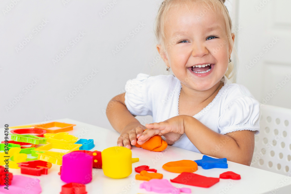 Toddler sculpts from colored plasticine on a white table. The hand of a small child squeezes pieces of colored plasticine. Childrens creativity, educational games, fine motor skills Toddler sculpts from colored plasticine on a white table. The hand of a small child squeezes pieces of colored plasticine. Childrens creativity, educational games, fine motor skills