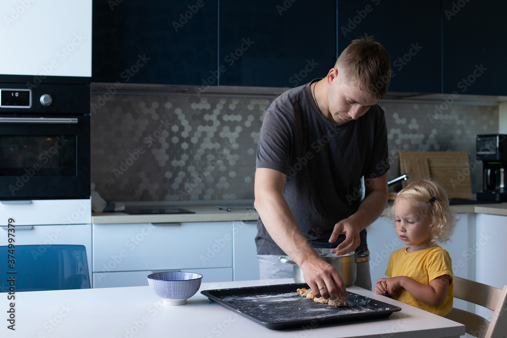 Young father and his small pretty daughter cooking together. Family is happily making cookies in the kitchen Young father and his small pretty daughter cooking together. Family is happily making cookies in the kitchen