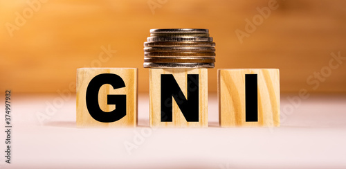 The concept of the word gni on wooden cubes with coins on a white wooden background. Business concept. GNI Gross national income photo