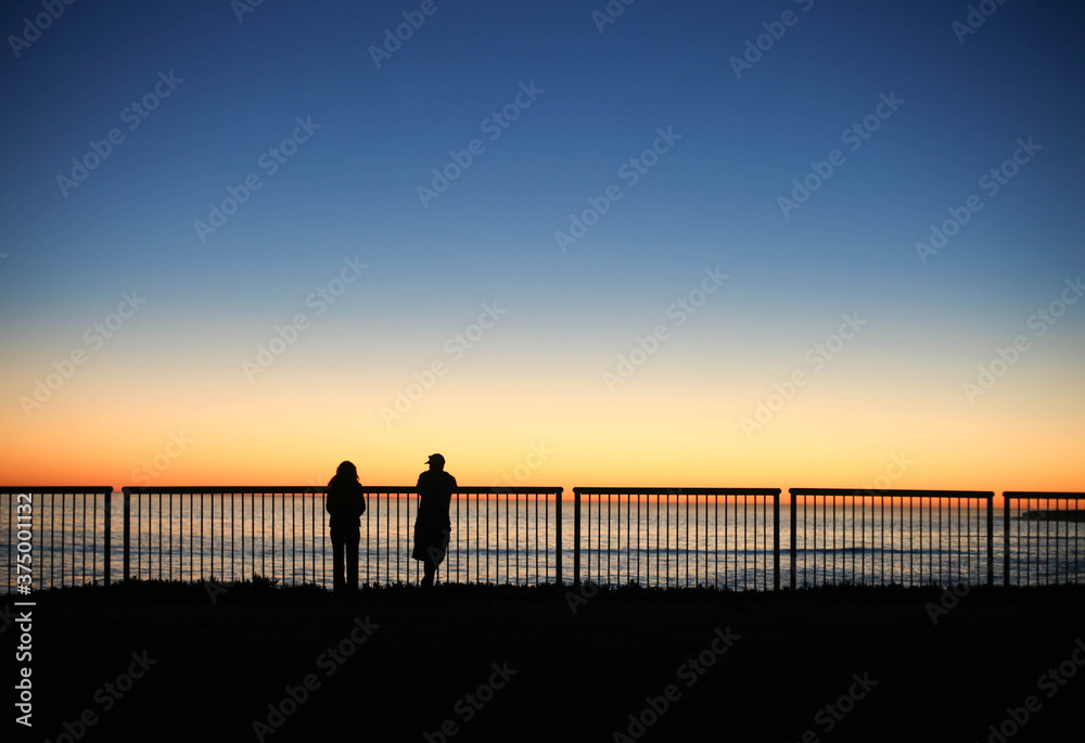 Male and female silhouettes watching the sun set over the ocean Male and female silhouettes watching the sun set over the ocean
