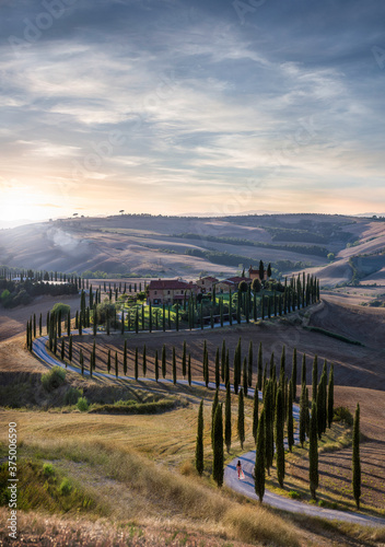 Sunset over beautiful S curved road in Tuscany, Italy - woman in red dress walking into distance