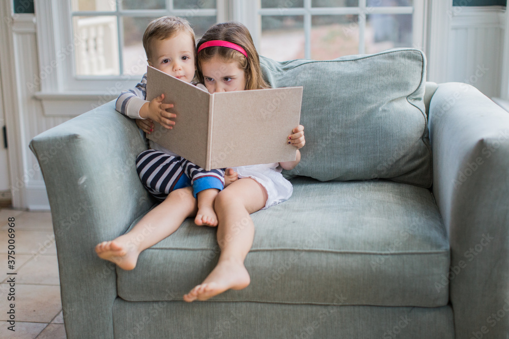 Young girl and boy toddler sitting on an oversized chair reading a book Young girl and boy toddler sitting on an oversized chair reading a book