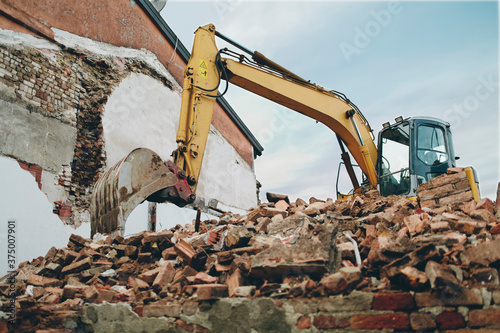 Below sight of yellow bulldozer dominating from top of ancient building ruins in Italy photo