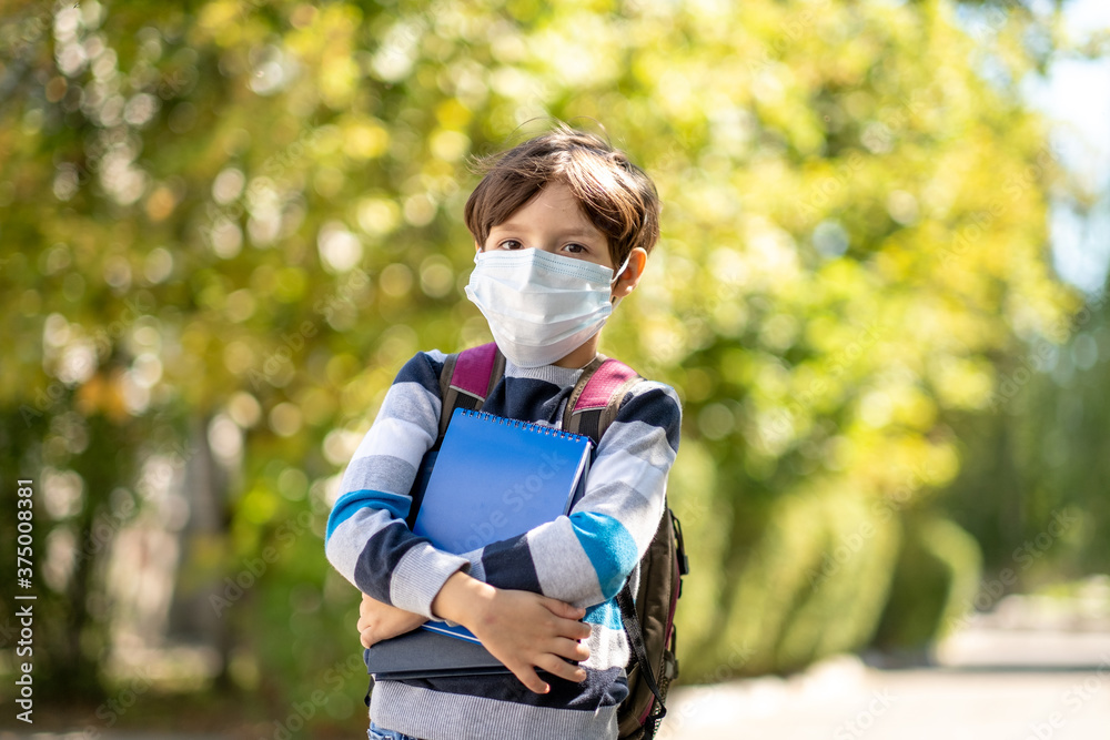 Coronavirus COVID-19 quarantine pandemic, portrait of a schoolboy wearing a protective mask outdoors in the open air. Child Little boy with a backpack going to school. Education. Health concept.