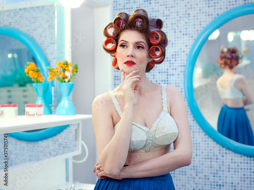 Portrait of vintage styled woman in a mid-century bathroom, with hair curlers in her hair. photo