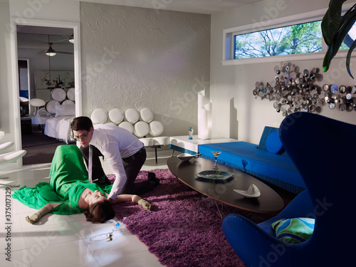 A man checking on a passed out woman in living room of a mid century modern home. photo