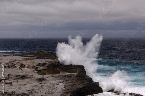 North coast of Gran Canaria, Canary Islands, Banaderos area, waves are breaking against elevated rock with salt evaporation ponds Salinas de Bufadero