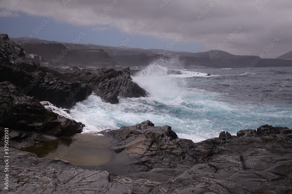 North coast of Gran Canaria, Canary Islands, Banaderos area, waves are breaking against elevated rock 
with salt evaporation ponds Salinas de Bufadero